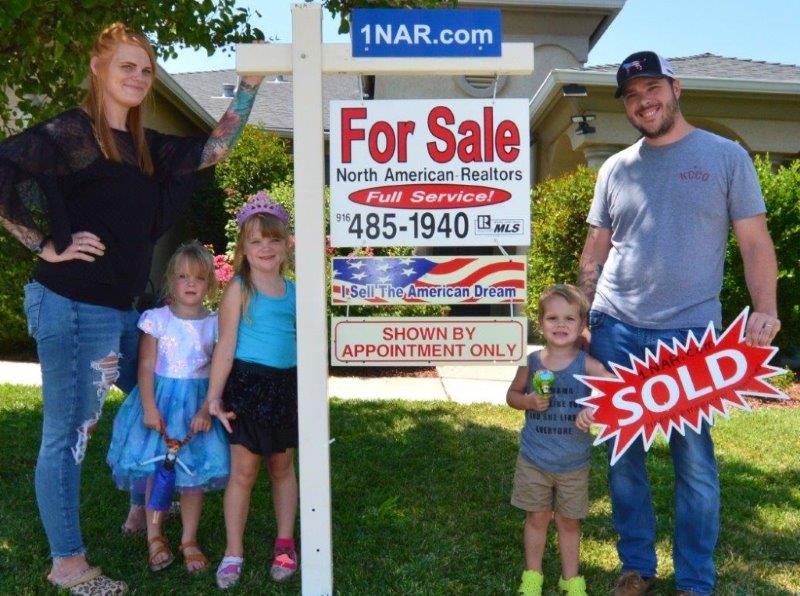 Sellers standing outside their home next to our real estate for sale sign holding a SOLD sign happy because the home is SOLD